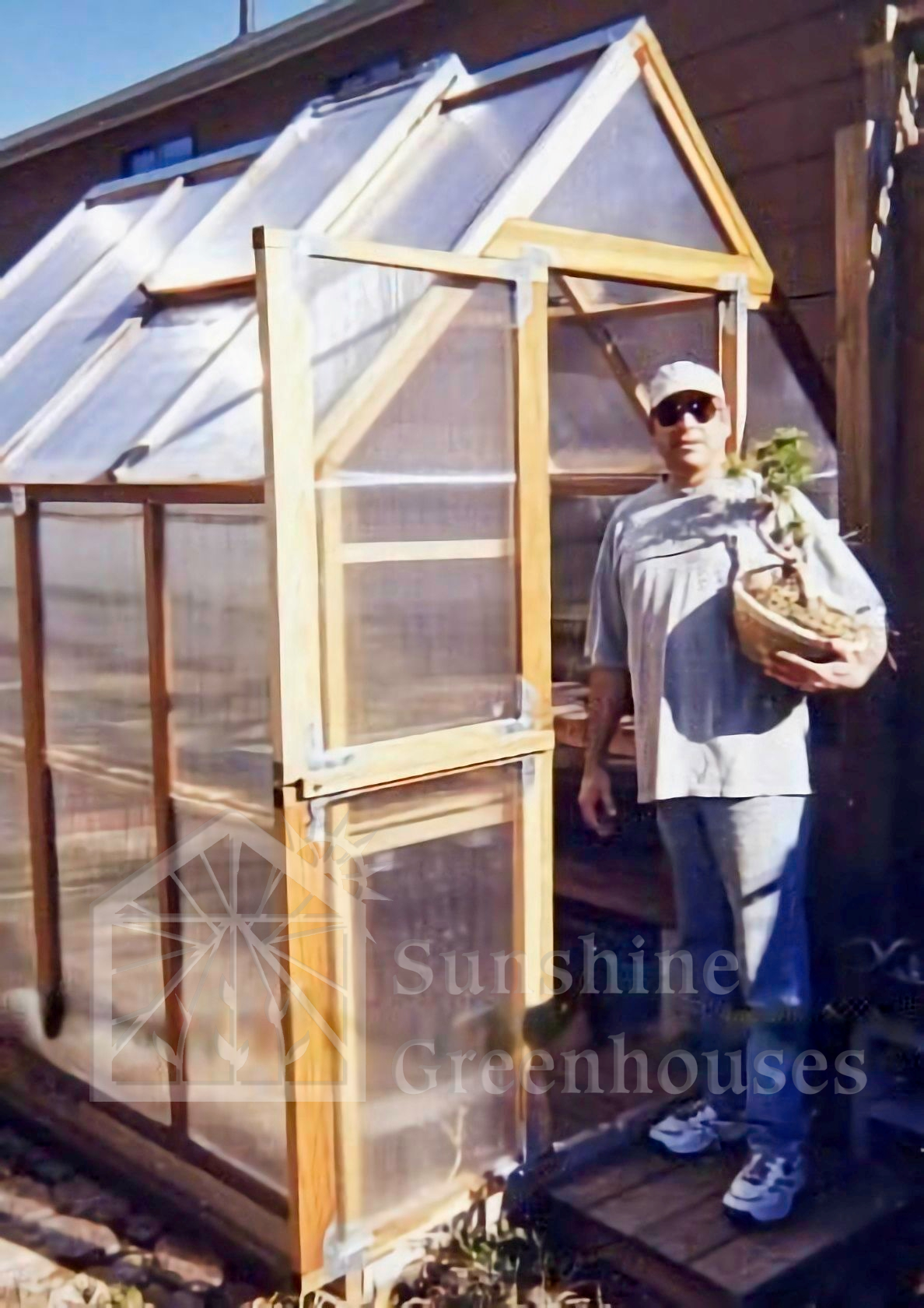 angle view of a 6 by 8 sunshine mt hood greenhouse kit, with customer holding plant from greenhouse